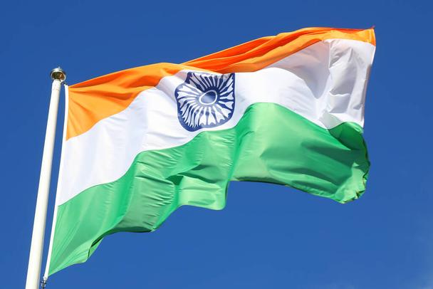 Close-up of the Indian flag waving in the wind against a blue sky.